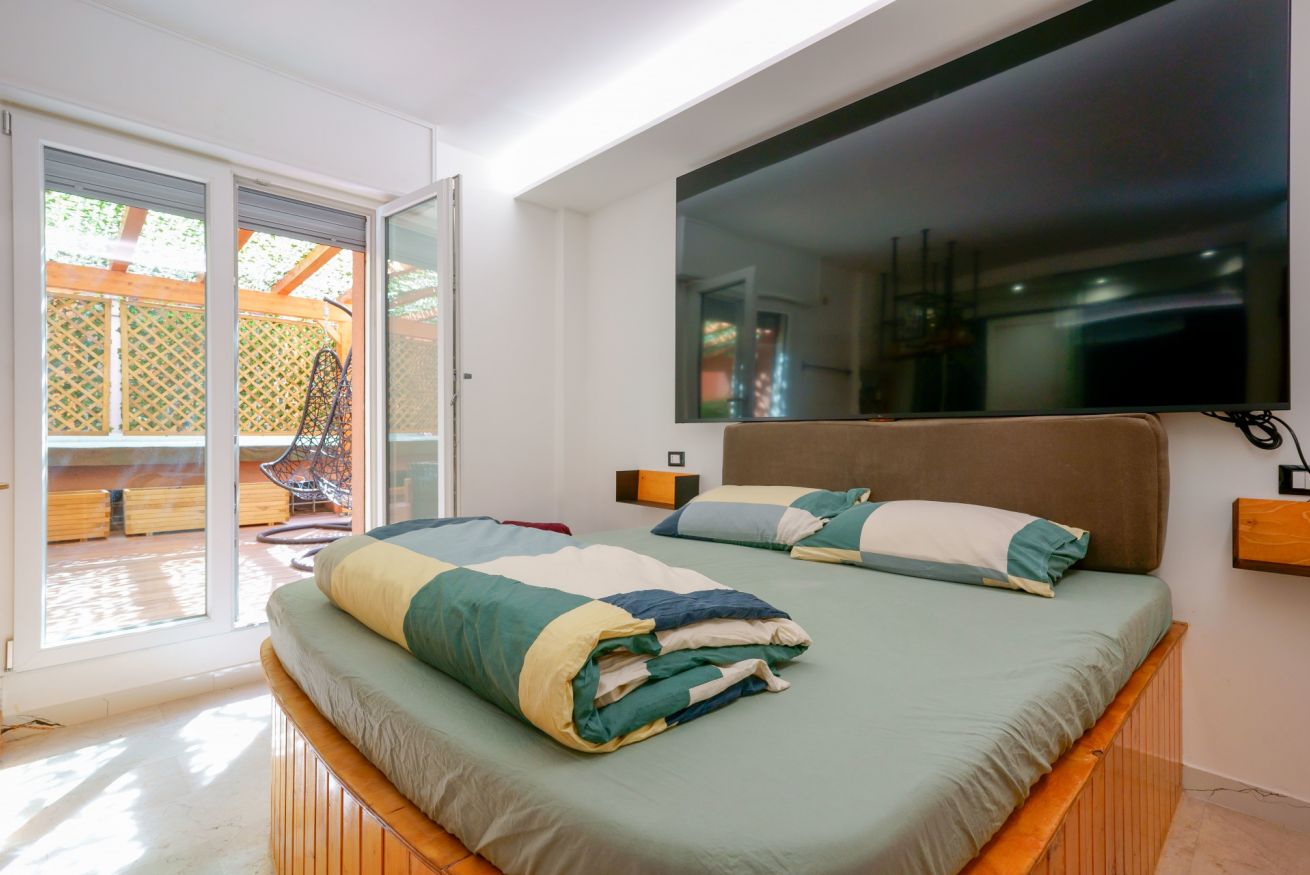 Camera matrimoniale luminosa con letto in legno, accesso diretto alla terrazza privata e grande specchio a parete che amplifica lo spazio.