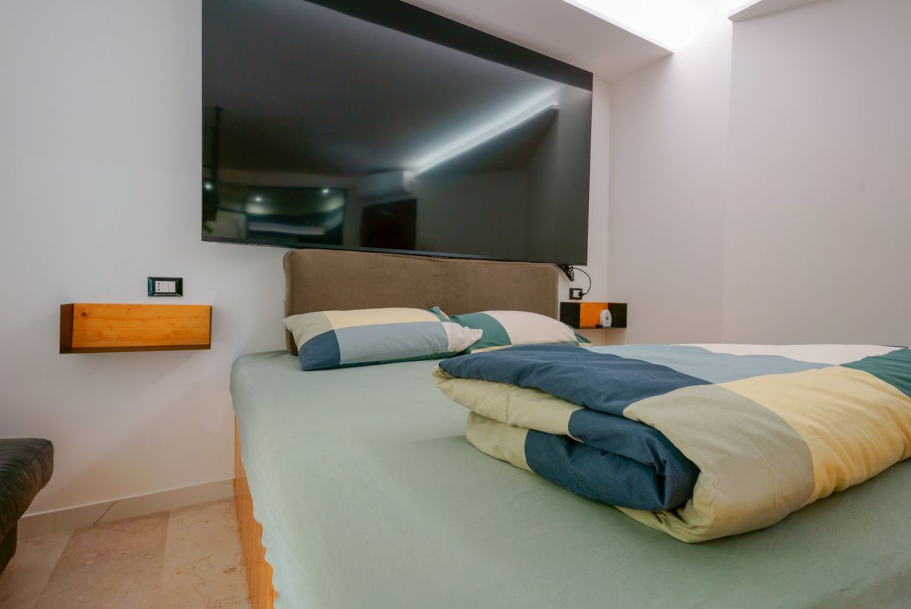 Camera matrimoniale con letto elegante, specchio a parete, illuminazione moderna e arredi essenziali che creano un'atmosfera accogliente e raffinata.