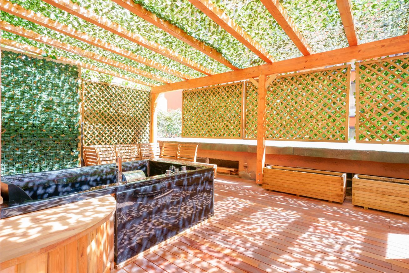 Terrazza privata con veranda in legno e pergolato verde, arredata con sedute confortevoli e illuminata naturalmente dalla luce solare filtrata.