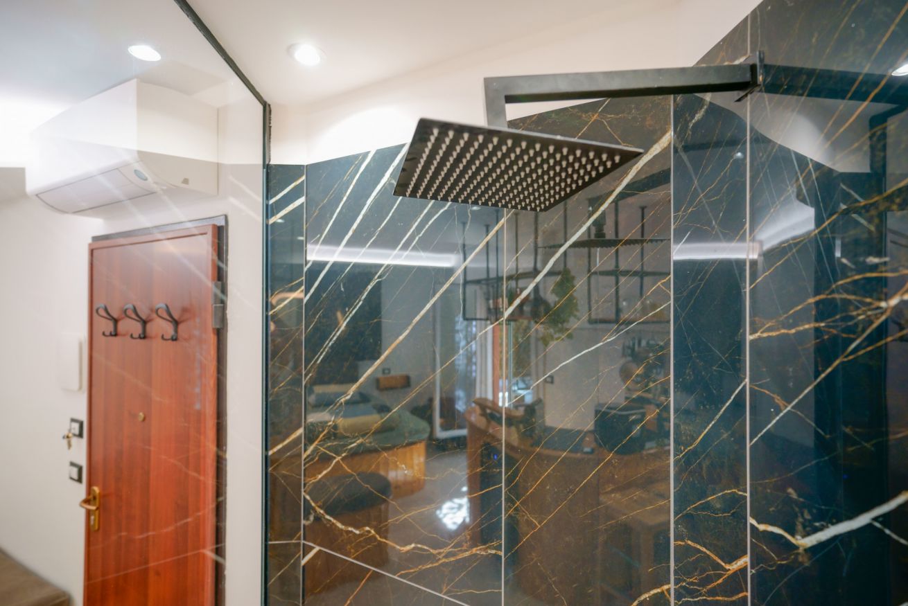 Bagno lussuoso con rivestimento in marmo nero e oro, doccia moderna con soffione a pioggia e dettagli di design contemporaneo.