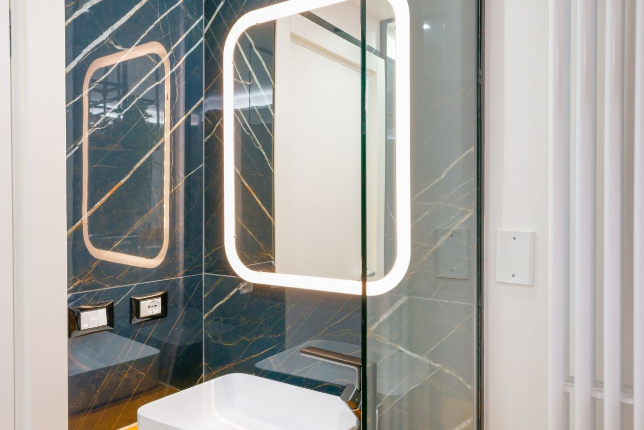 Bagno elegante con rivestimenti in marmo scuro e specchio illuminato, che riflette il lusso e il comfort della Camera Deluxe.