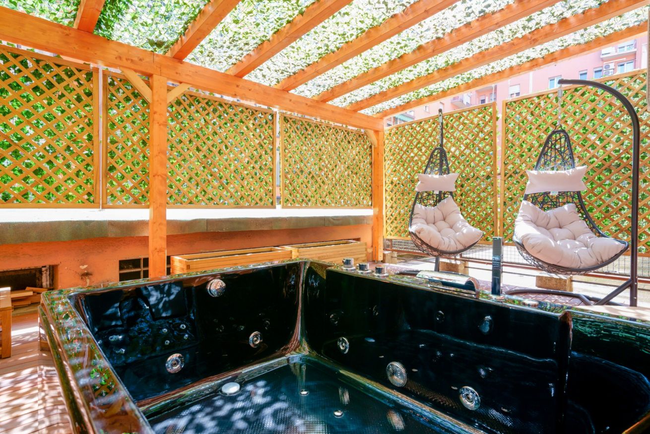 Terrazza privata con vasca idromassaggio, pergolato in legno e verde rigoglioso: il rifugio perfetto per relax indimenticabile.