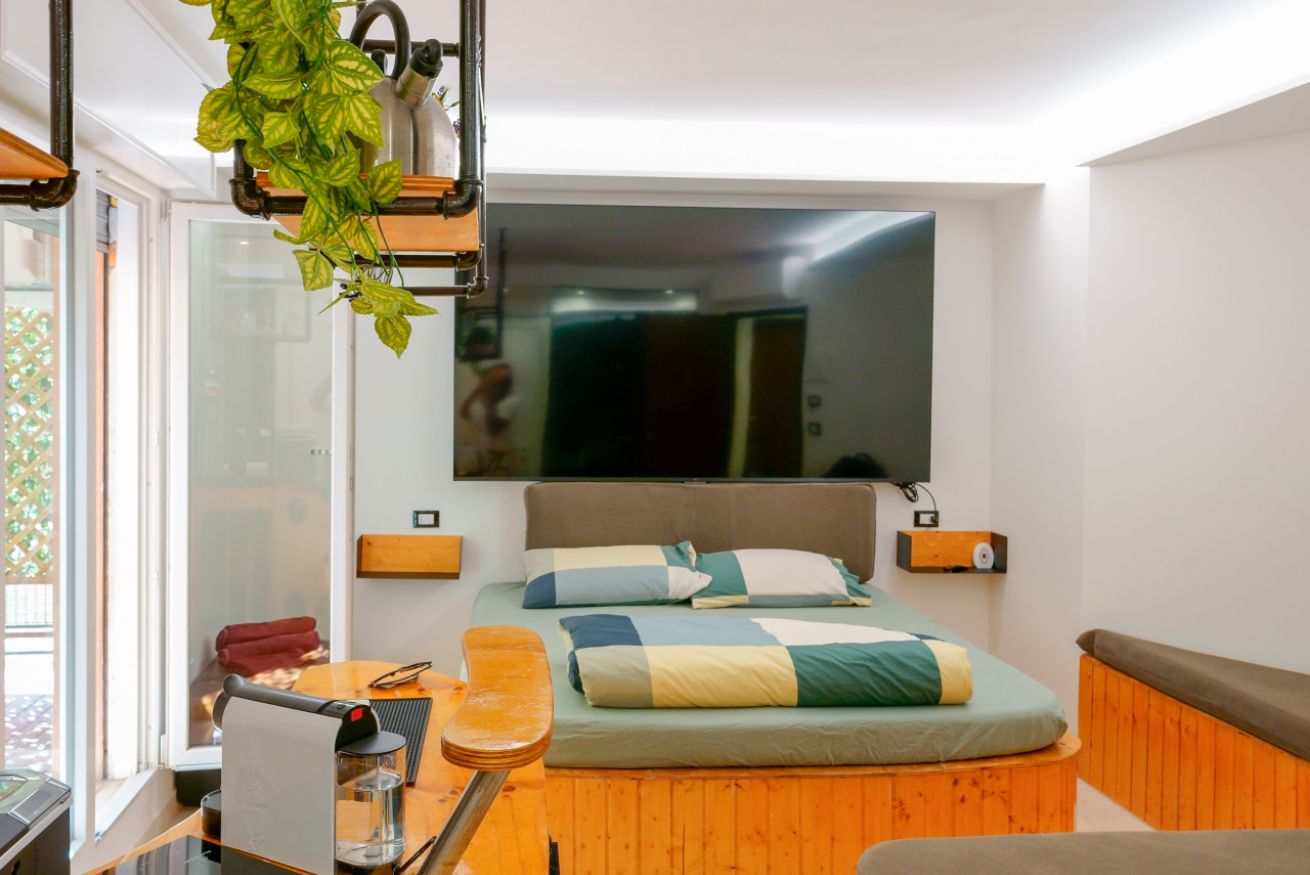 Camera matrimoniale luminosa con letto elegante, testata in legno, arredi moderni in tonalità calde e accesso diretto alla terrazza privata.
