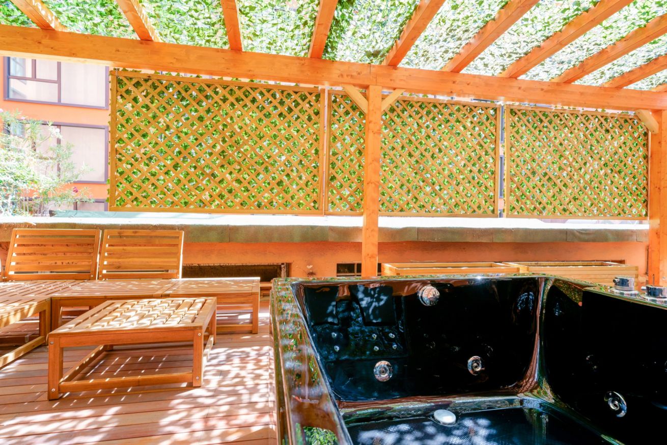 Una terrazza esclusiva con pergolato in legno e vasca idromassaggio privata, circondata dal verde e dalla luce naturale che filtra delicatamente.