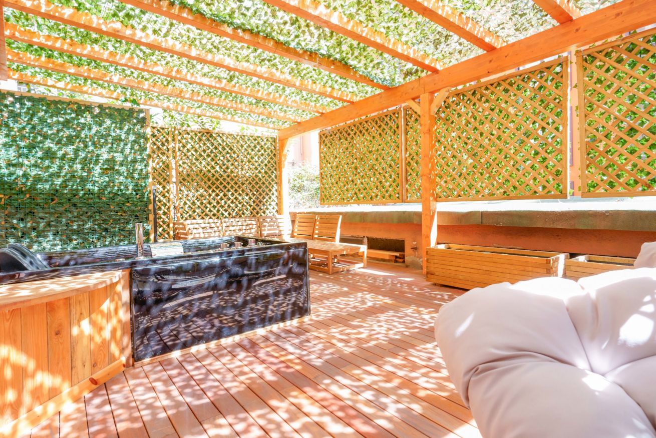 Terrazza privata con pergolato e vegetazione rigogliosa, arredata con comfort: divano bianco, tavolo in legno e zona living all'aperto.