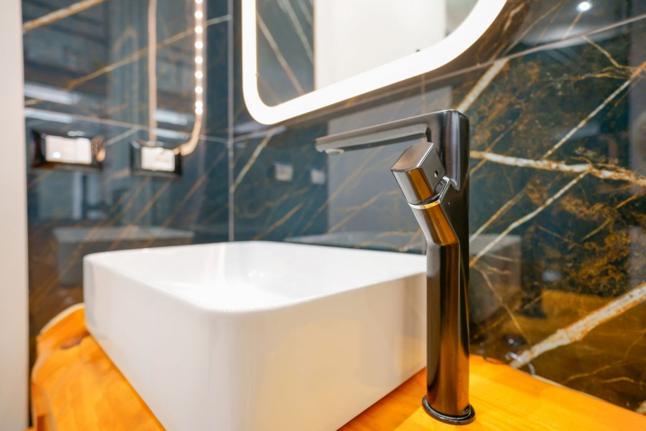 Elegante lavabo in ceramica bianca su piano in marmo nero, con miscelatore design e specchio illuminato: il bagno deluxe che merita.