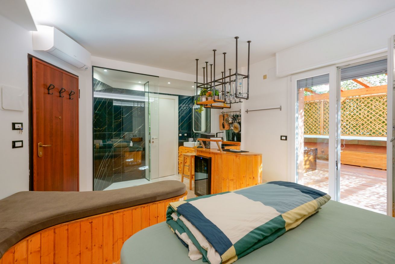 Elegante camera matrimoniale con letto in ferro battuto, arredo in legno caldo e accesso diretto alla terrazza privata con vista sul giardino.