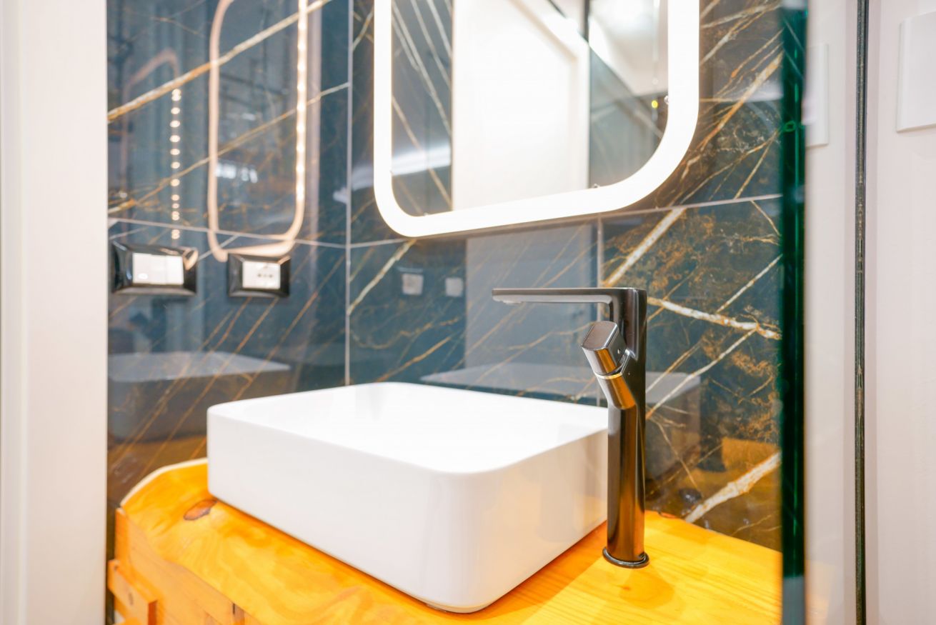 Elegante bagno con lavabo di design su base gialla, specchio illuminato e piastrelle marmorizzate: lusso e modernità a portata di mano.
