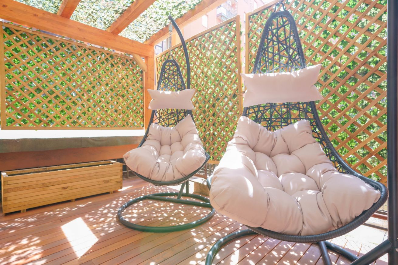 La terrazza privata si trasforma in oasi di relax con le sue comode sedie sospese, circondata da verdure rigogliose e illuminata da una luce naturale avvolgente.