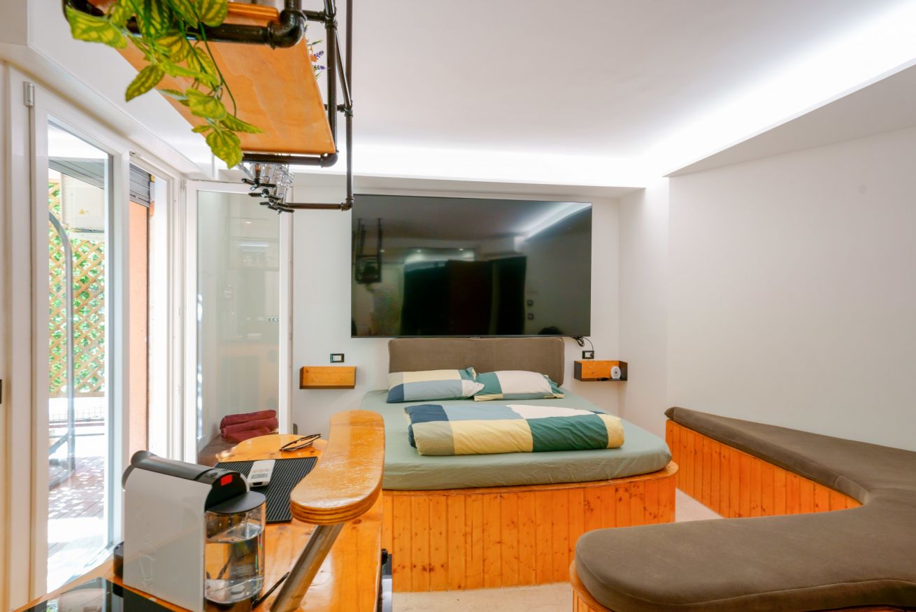 Camera matrimoniale elegante con accenti arancioni, TV integrata, letto con testata rivestita e accesso diretto alla terrazza privata.