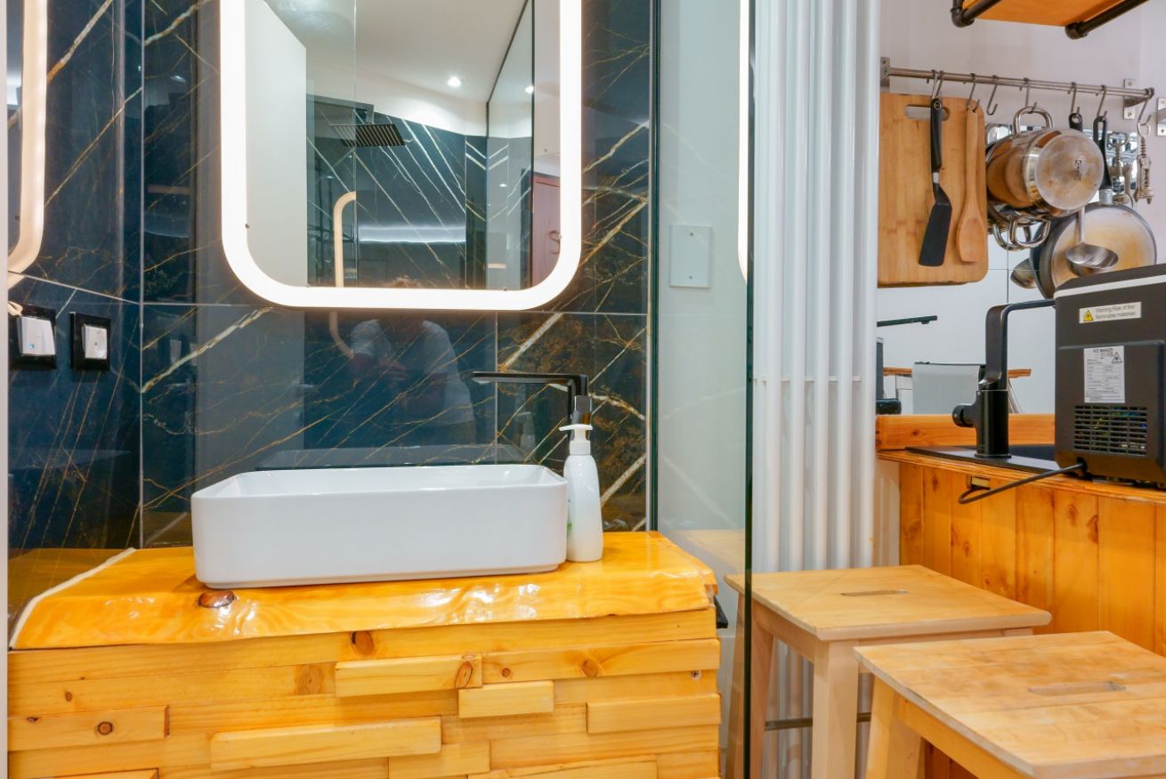 Bagno raffinato con lavabo su base in legno naturale, specchio illuminato e piastrelle blu scuro: eleganza e comfort in ogni dettaglio.