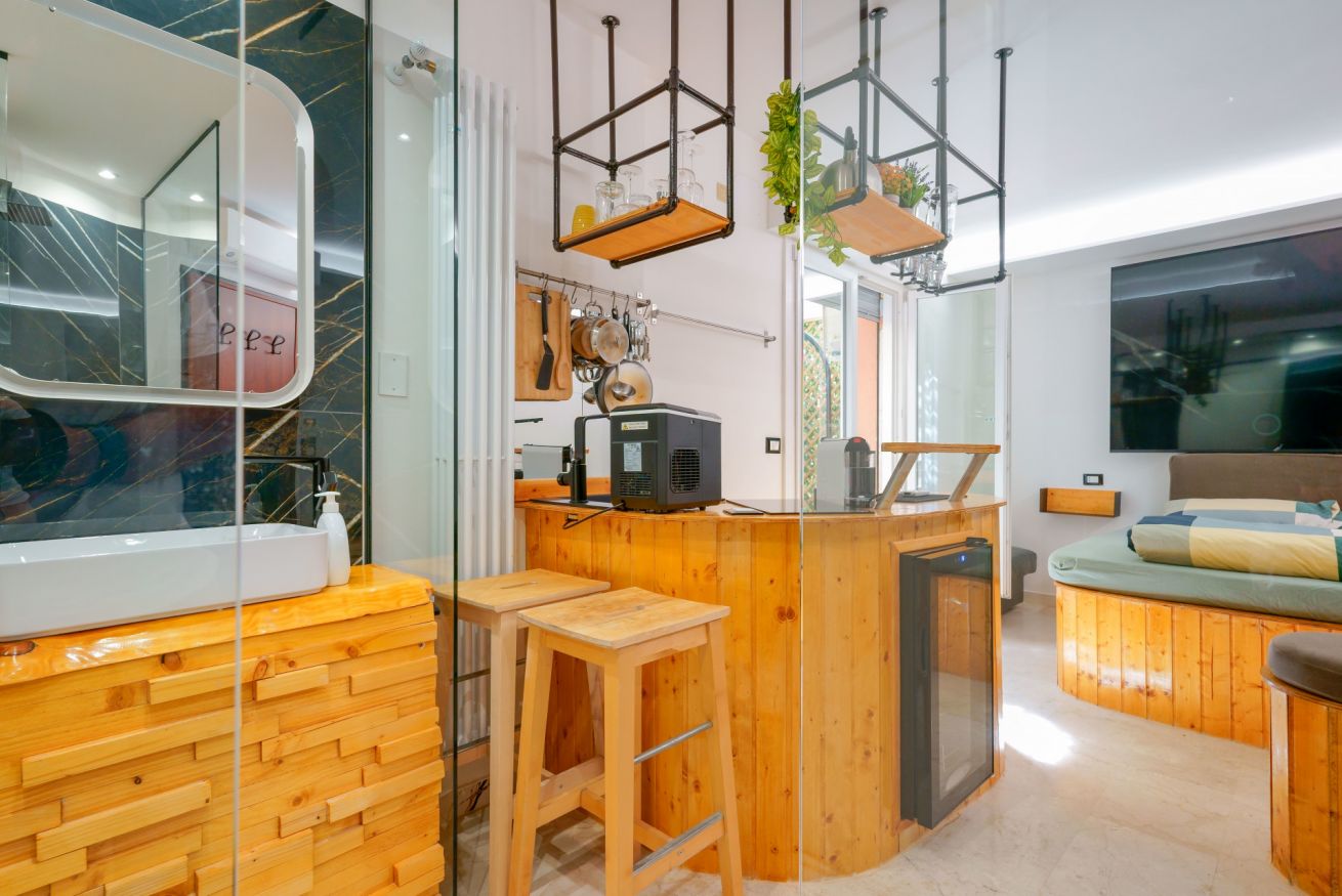 Elegante zona living con arredamento in legno naturale, bancone con sgabelli, lampadari moderni e ampi spazi luminosi per un soggiorno raffinato.