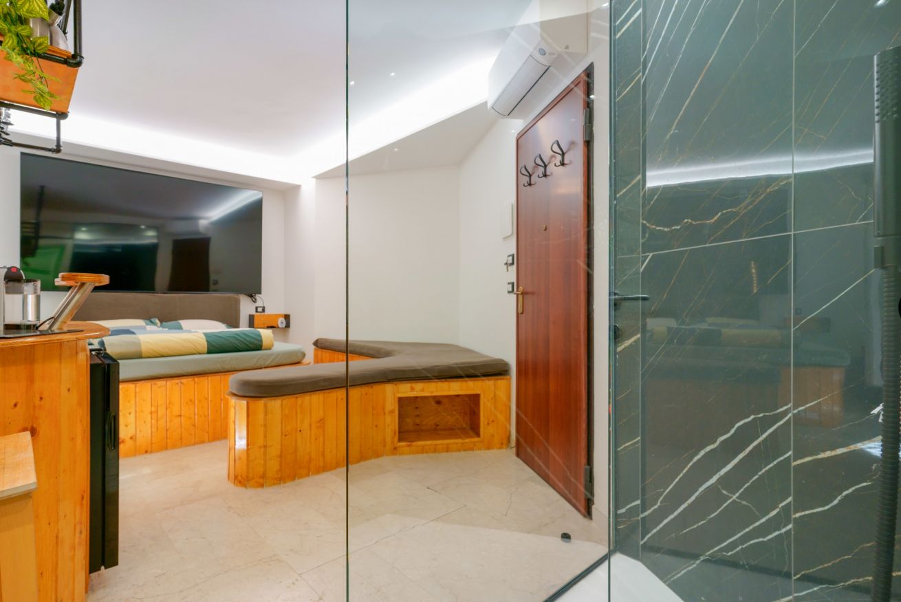 Bagno elegante con legno naturale, vasca spa integrata e doccia in vetro con rivestimento in marmo verde, illuminazione zen e specchio ampio.