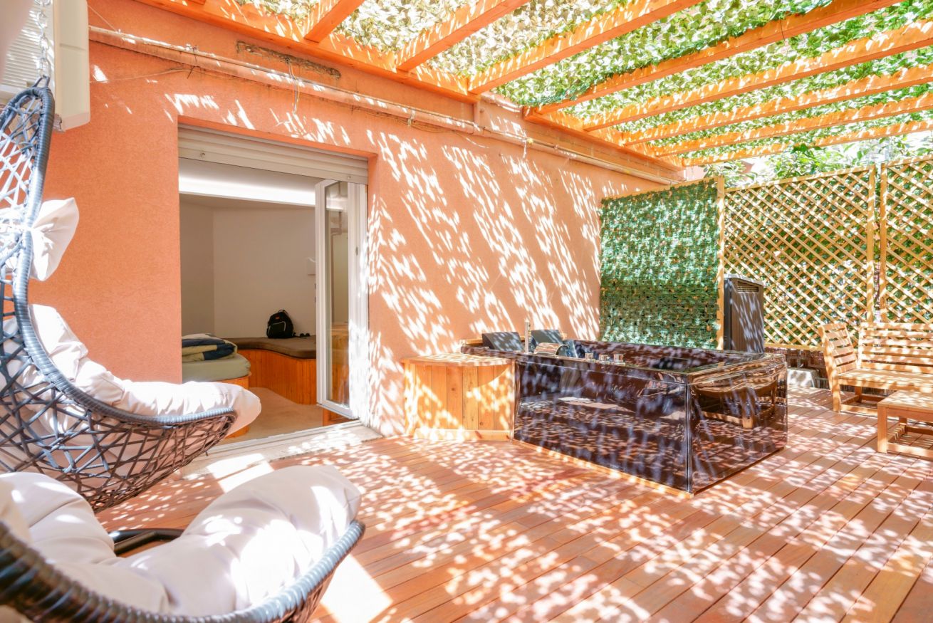 Terrazza privata luminosa con pergolato verde, arredamento elegante e morbidi cuscini: il rifugio perfetto per rilassarsi sotto il sole.