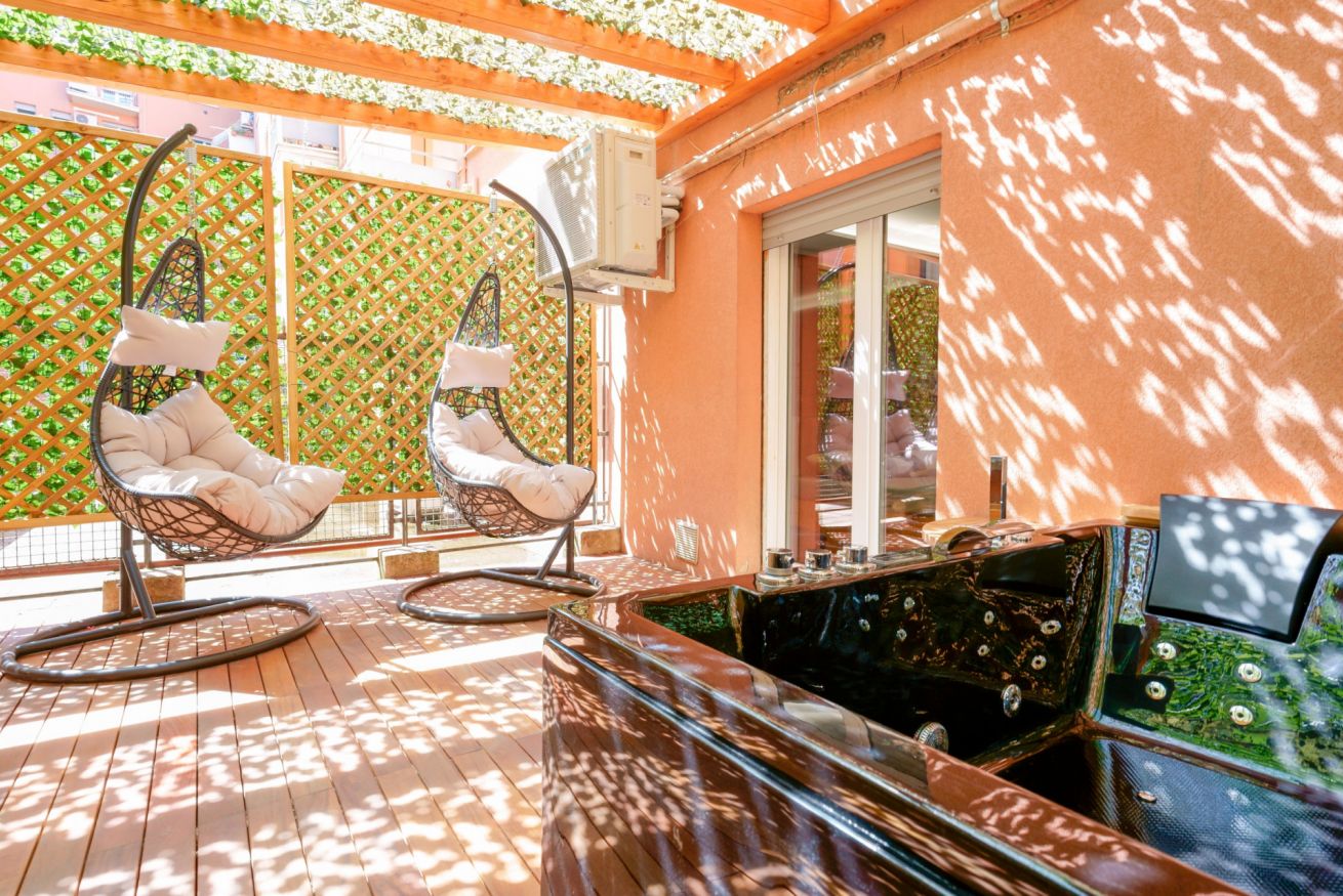 Terrazza privata con amaca sospesa immersa nella luce naturale, circondata da verde rigoglioso e architettura in cotto toscano.