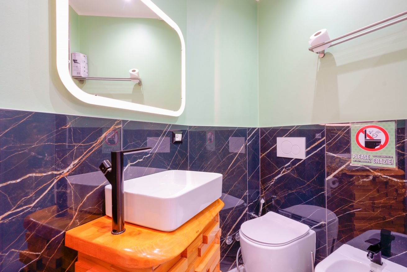 Bagno elegante con rivestimenti in marmo scuro, mobile lavabo arancione design e specchio luminoso: comfort e stile per momenti di relax.