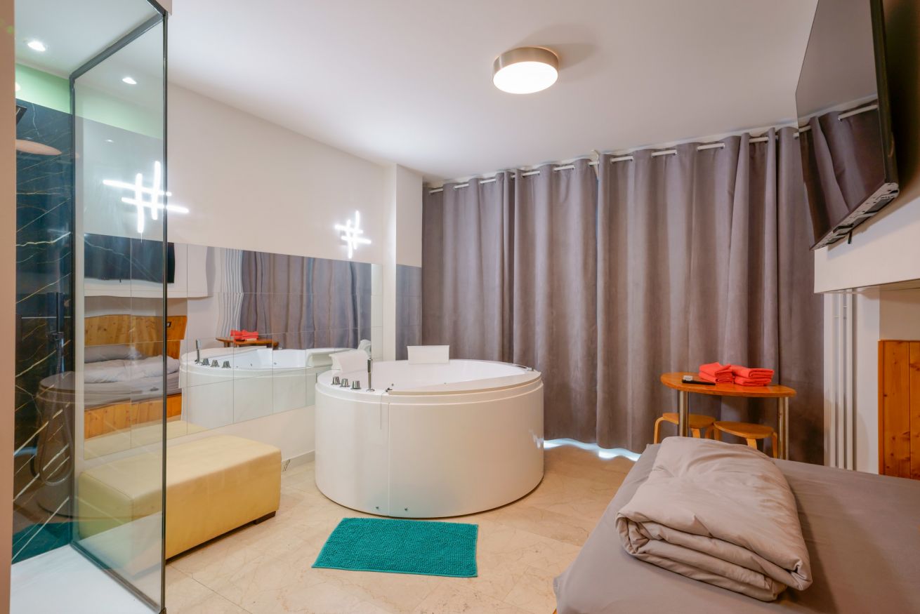 Camera matrimoniale con vasca idromassaggio circolare, bagno en-suite con doccia in vetro e arredi eleganti in toni neutri e legno naturale.