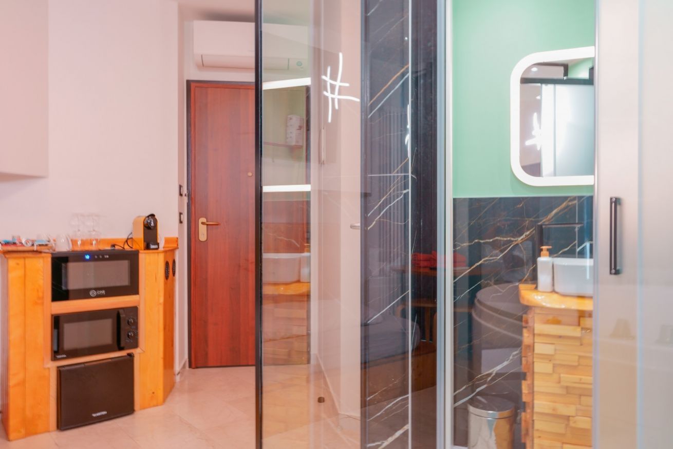 Moderna camera matrimoniale con angolo cottura arancione, bagno con vasca idromassaggio e doccia, finiture eleganti in marmo e tonalità rilassanti.