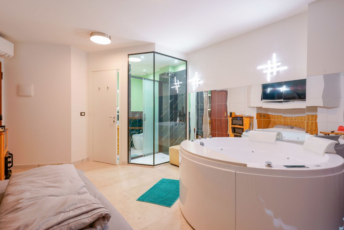 Camera spaziosa con vasca idromassaggio circolare, doccia walk-in moderna e arredi eleganti per un soggiorno di lusso e relax.