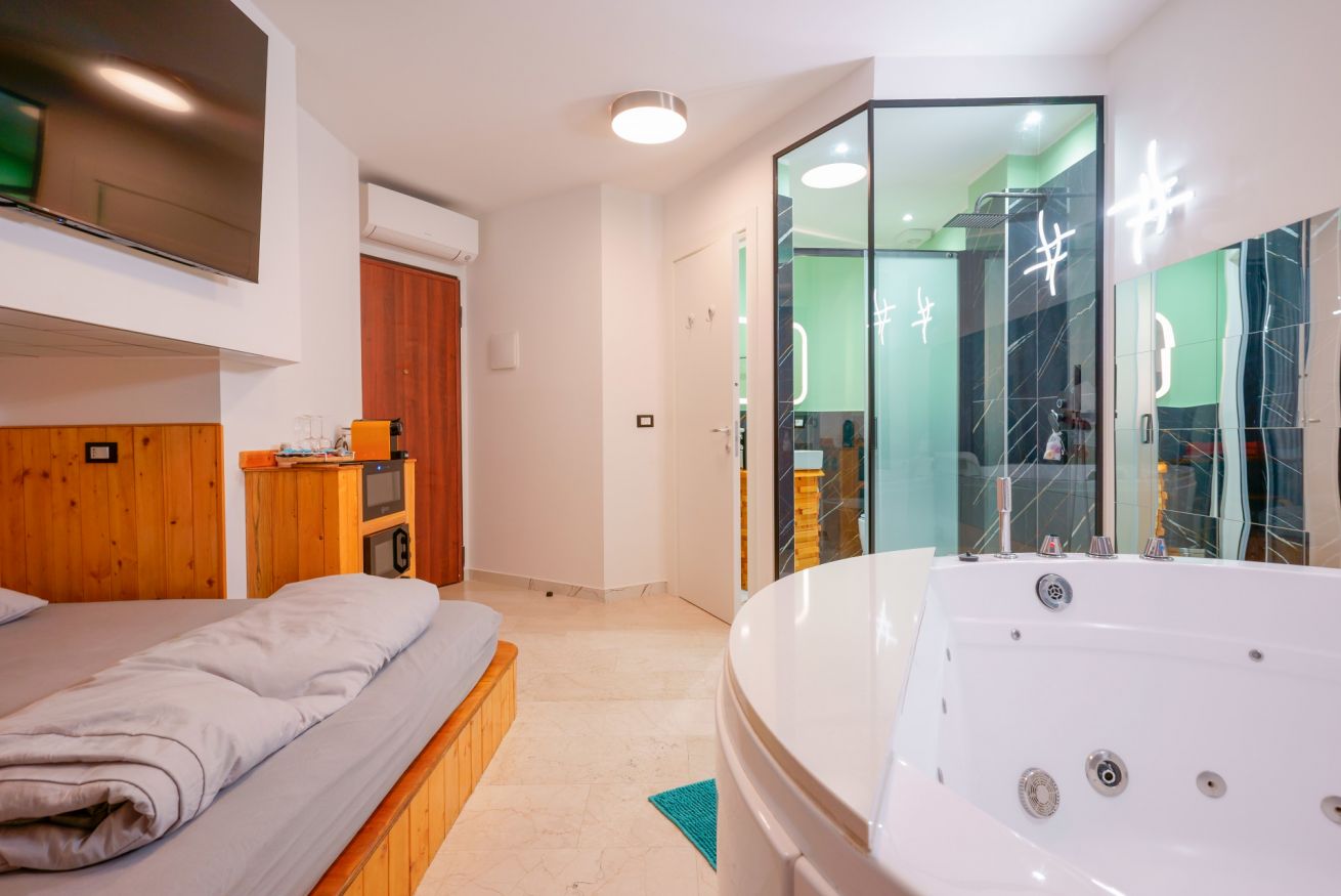 Camera matrimoniale elegante con vasca idromassaggio a 2 posti, doccia in vetro e letto in legno, perfetta per un relax indimenticabile.