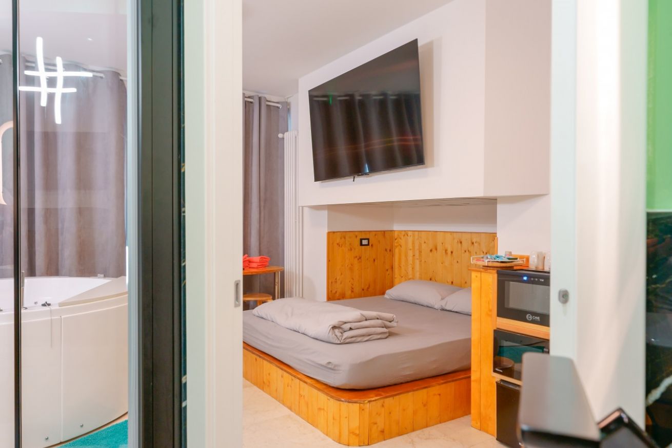 Camera accogliente con letto matrimoniale in legno, vasca idromassaggio privata, TV a parete e arredi funzionali per un soggiorno confortevole e rilassante.