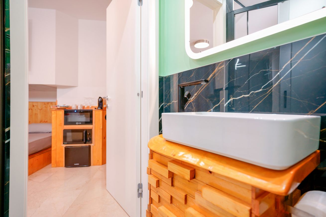 Elegante camera matrimoniale con vasca idromassaggio in legno, specchio illuminato e rivestimenti in marmo nero per un'atmosfera di lusso e relax.