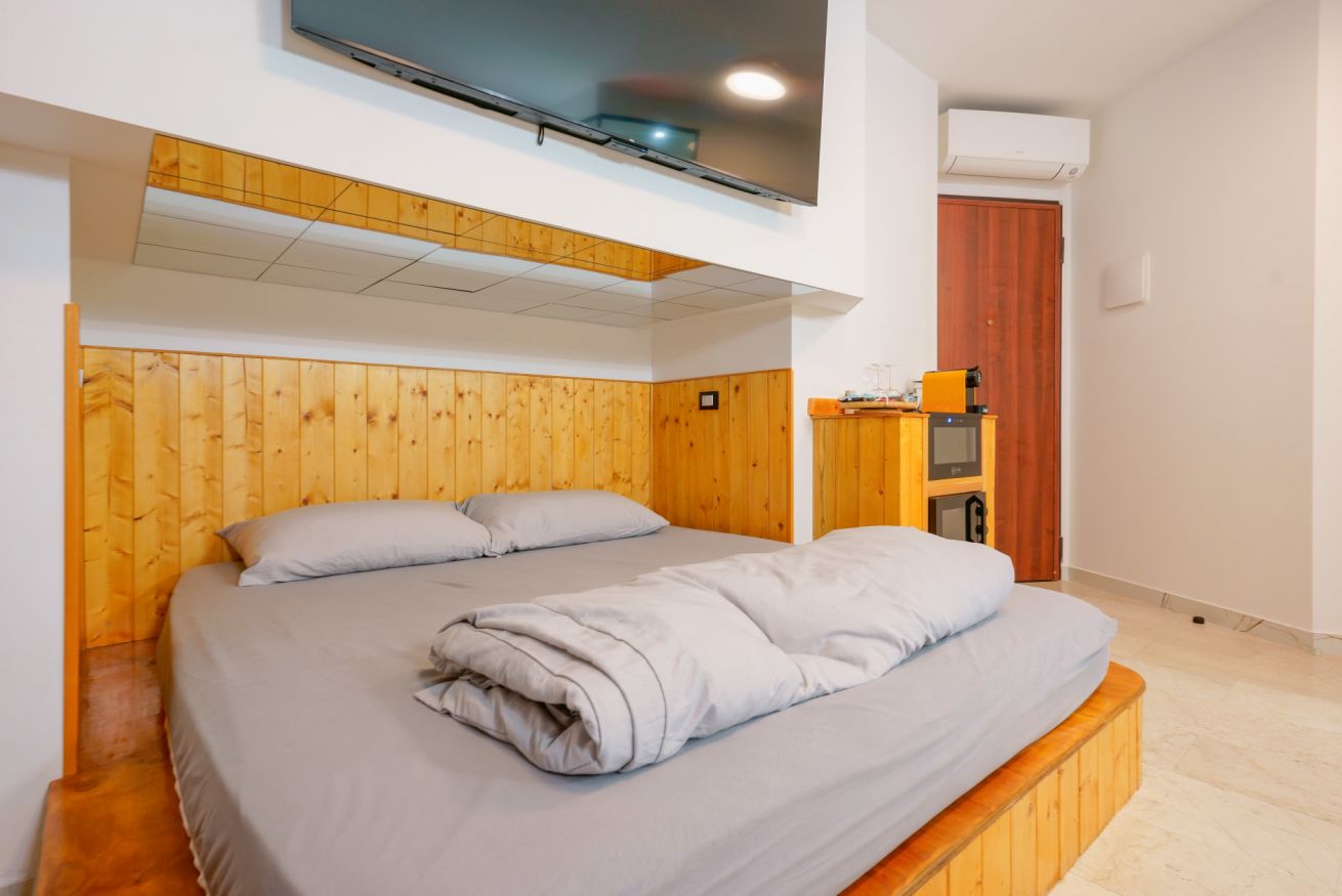 Camera matrimoniale accogliente con letto in legno, arredamento moderno e funzionale, grande TV e ampio spazio luminoso per il vostro comfort.