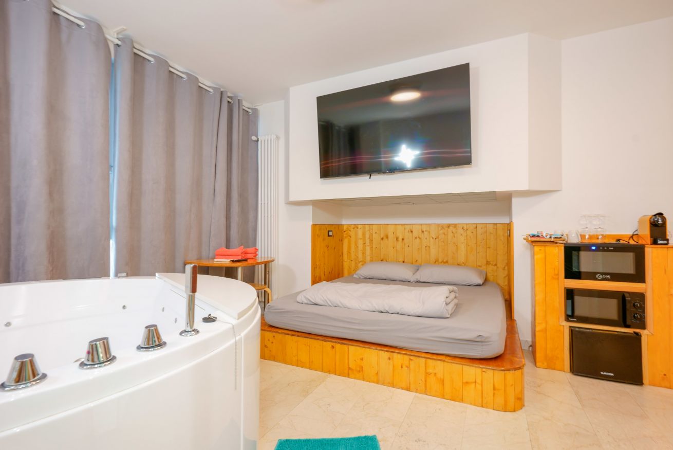 Camera accogliente con vasca idromassaggio a 2 posti, letto matrimoniale in legno e moderna dotazione di intrattenimento, perfetta per un soggiorno rilassante.