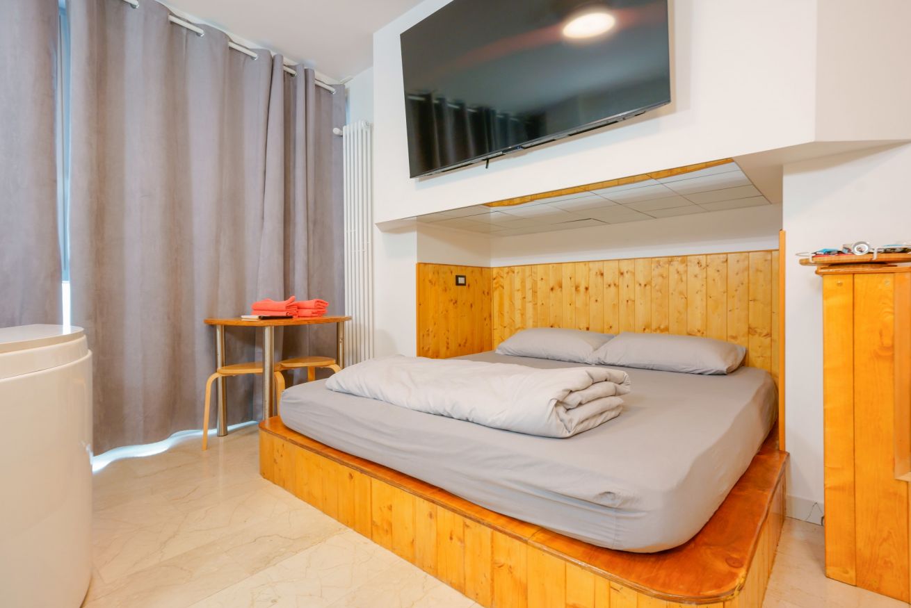 Camera matrimoniale accogliente con letto in legno, TV integrata e arredo moderno in tonalità calde, perfetta per un soggiorno confortevole e rilassante.