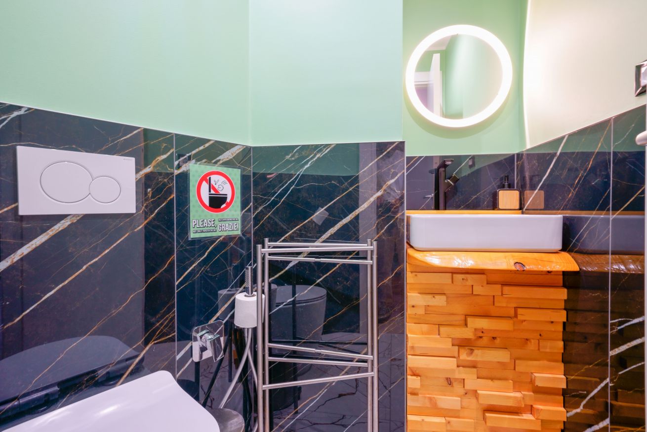 Modern bathroom featuring elegant dark marble finishes, illuminated mirror and practical amenities, ensuring perfect comfort for your stay.