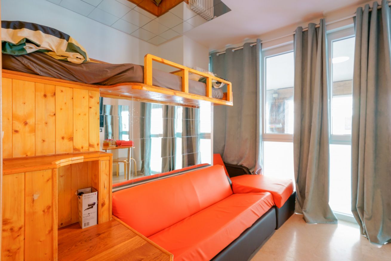 Bright room with a red double bed, natural wood furnishings, and expansive window views: comfort and warmth in every detail.