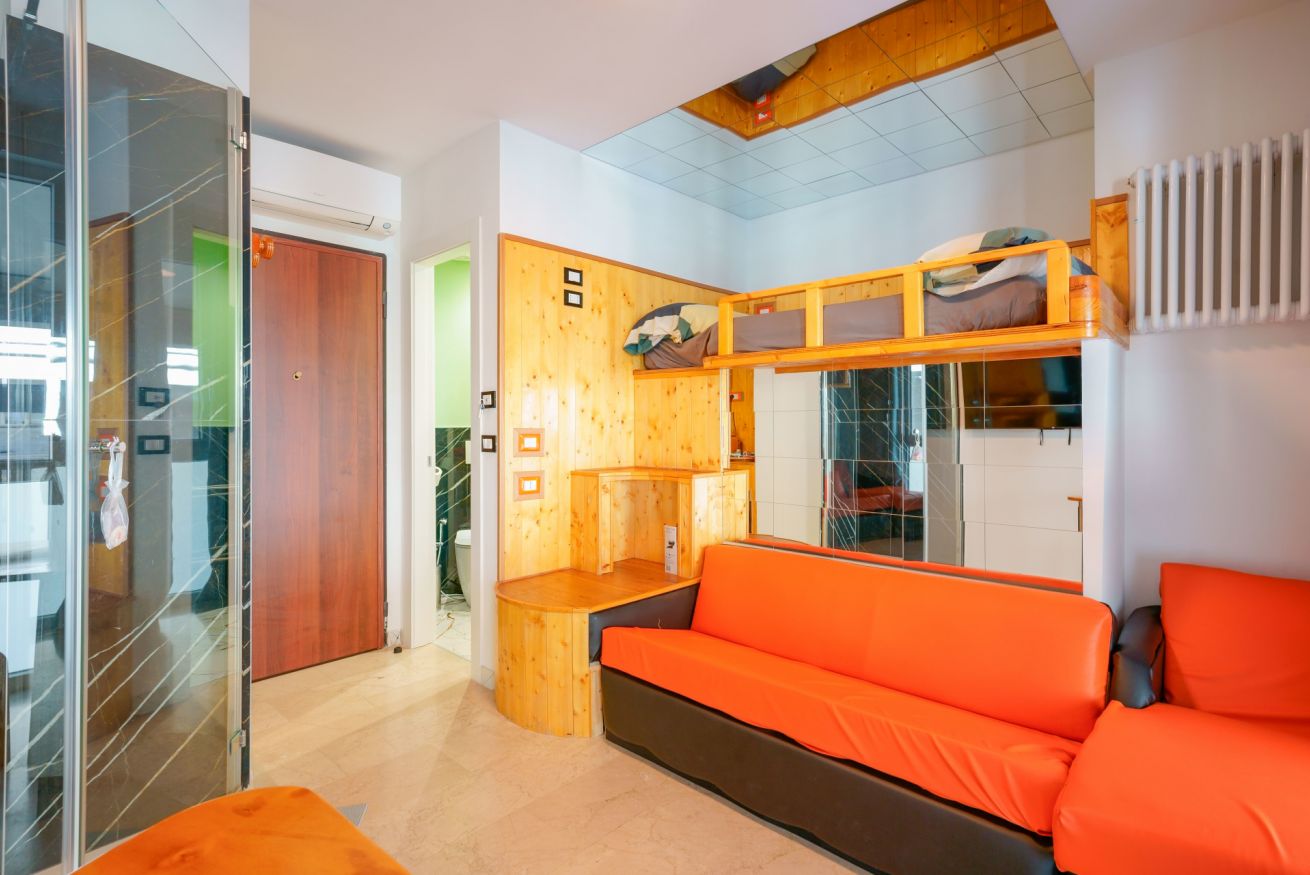 A bright and welcoming room featuring modern natural wood furnishings, a vibrant orange-toned sofa, and thoughtfully organized spaces designed for maximum comfort.
