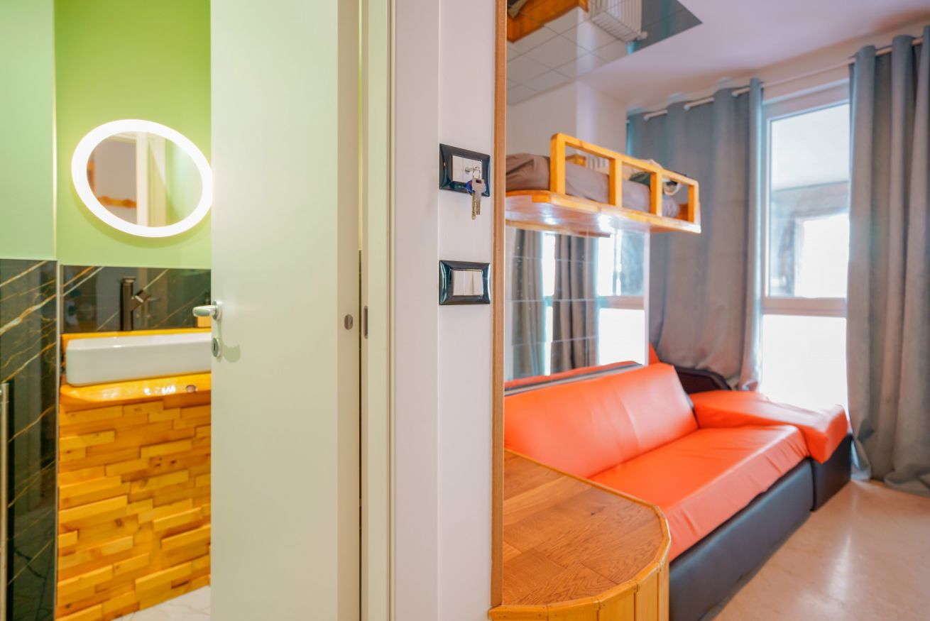 Camera accogliente con letto singolo in arancio vivace, bagno privato con specchio illuminato e finestre luminose per una permanenza confortevole.