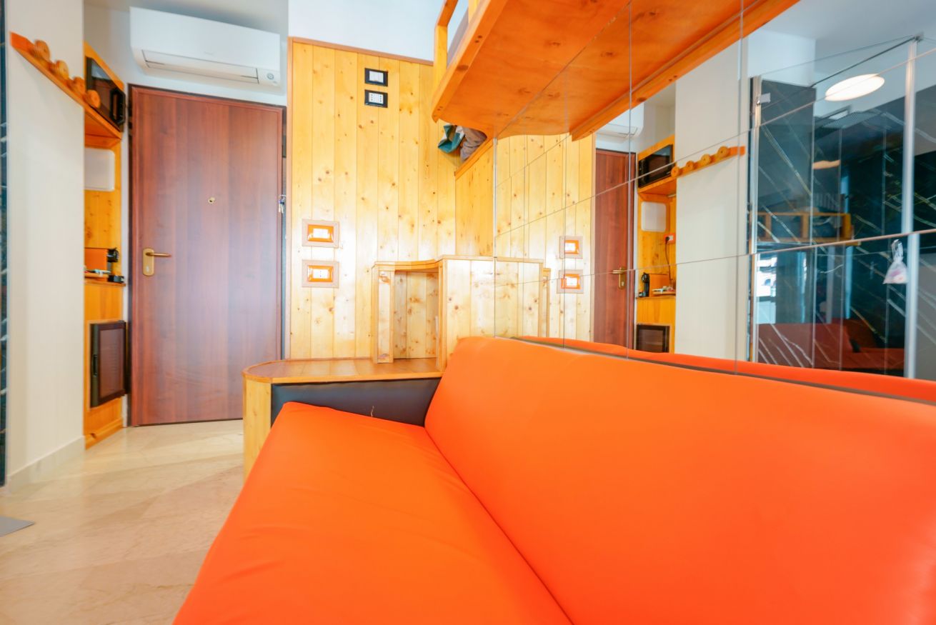 Camera singola luminosa con letto confortevole in arancio vivace, soffitti in legno, arredi moderni e ampi spazi funzionali per una permanenza piacevole.